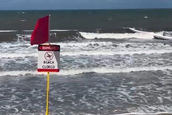 A sign and flag on a beach reading "Danger, Beach Closed"
