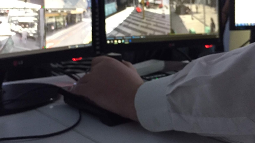 A hand on a joy stick and CCTV screens showing surveillance of Brisbane city.