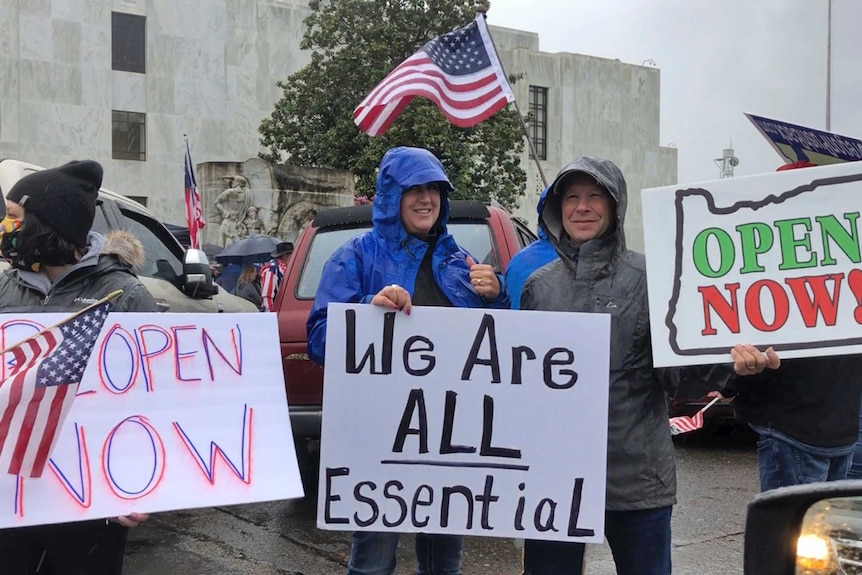 People wearing rain jackets hold up placards protesting against coronavirus restrictions.