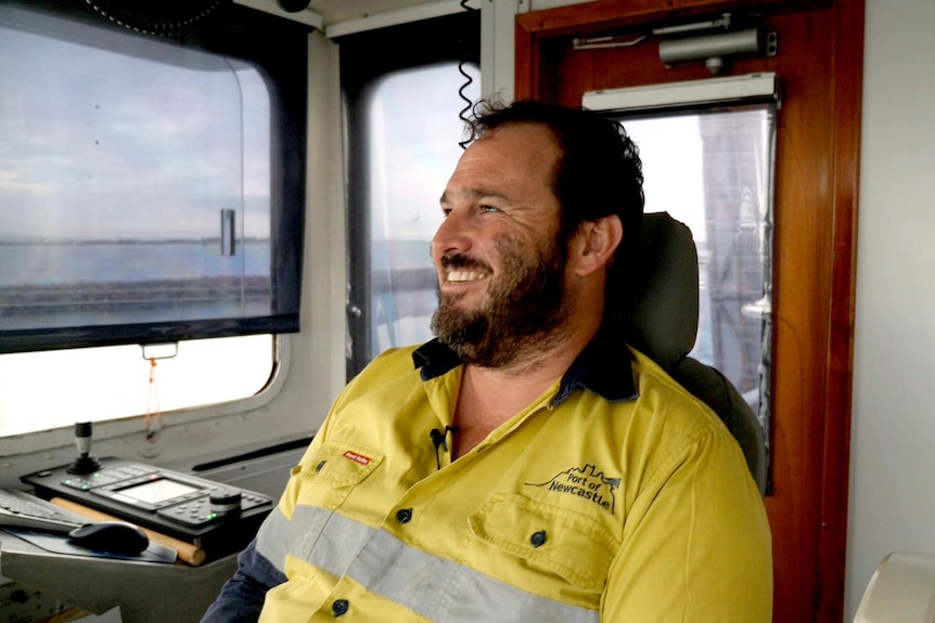 A smiling dredge master in a hi vis shirt on the bridge of his ship.