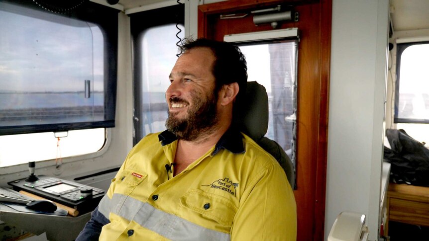 A smiling dredge master in a hi vis shirt on the bridge of his ship.