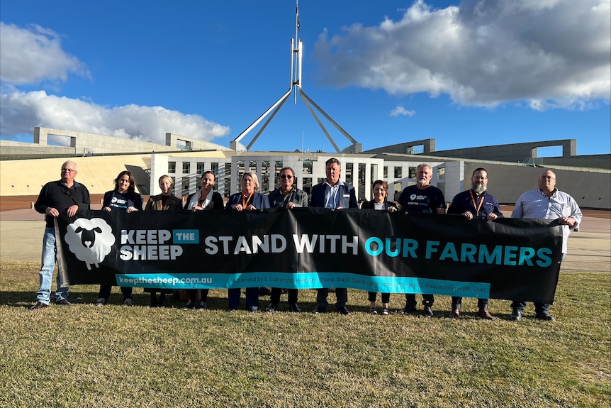 A group of people stand outside Canberra parliament house holding a banner reading "Keep The Sheep: Stand with our farmers".