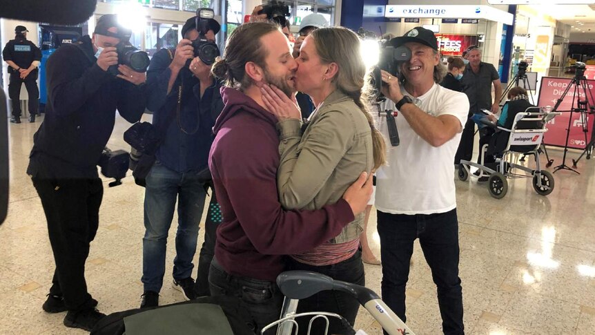 A couple kiss in front of photographers