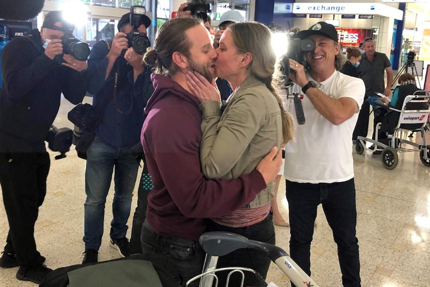 A couple kiss in front of photographers