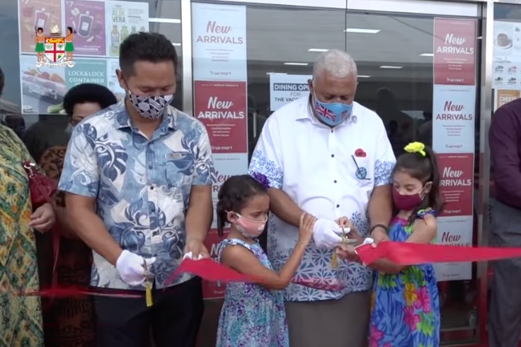 Daniel Kim and Frank Bainimarama cut a ribbon together at a supermarket opening with two young girls. 