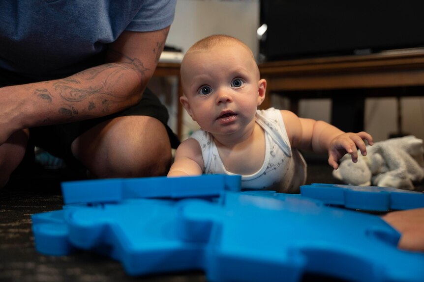 A baby lies on the floor with jigsaw puzzle pieces.