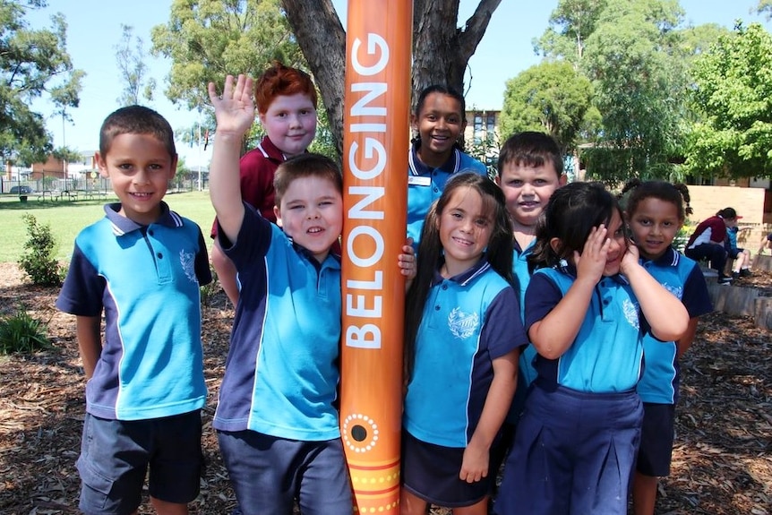 Several smiling children stand around a pole with the word belonging written on it.
