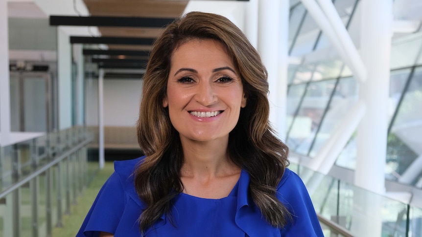 Patricia Karvelas stands next to windows, smiling at the camera. 
