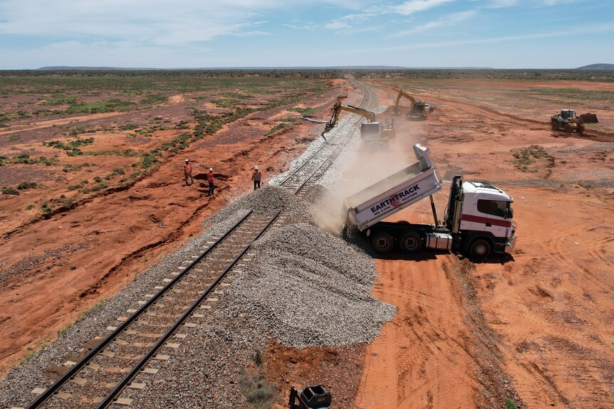 a drone shot of a truck tipping rubble onto the edge of a damaged rail line.