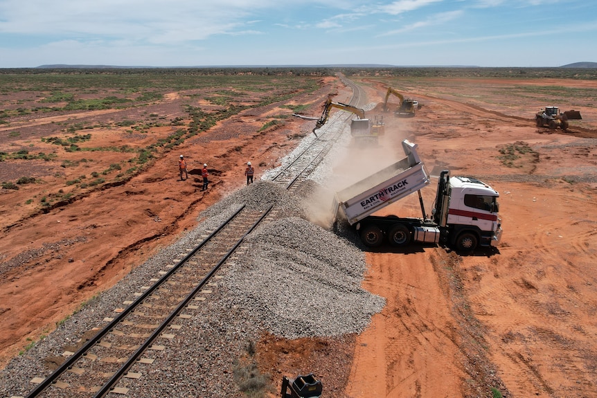 a drone shot of a truck tipping rubble onto the edge of a damaged rail line.