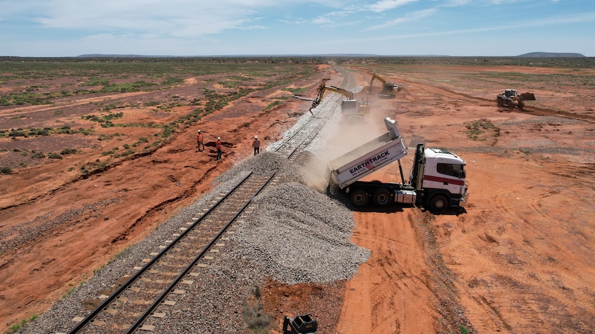 a drone shot of a truck tipping rubble onto the edge of a damaged rail line.