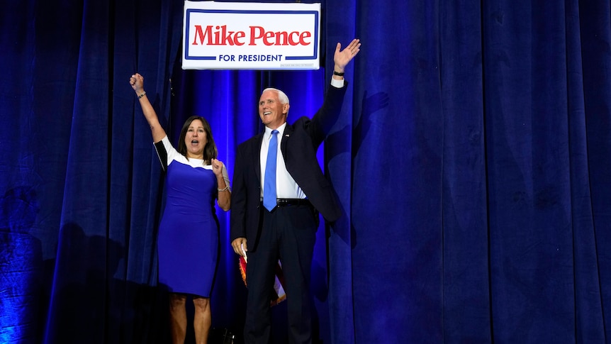 Man and woman wave and cheer walking out from behind blue curtain.