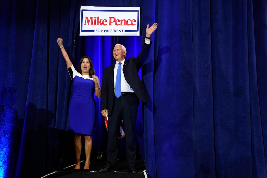 Man and woman wave and cheer walking out from behind blue curtain.