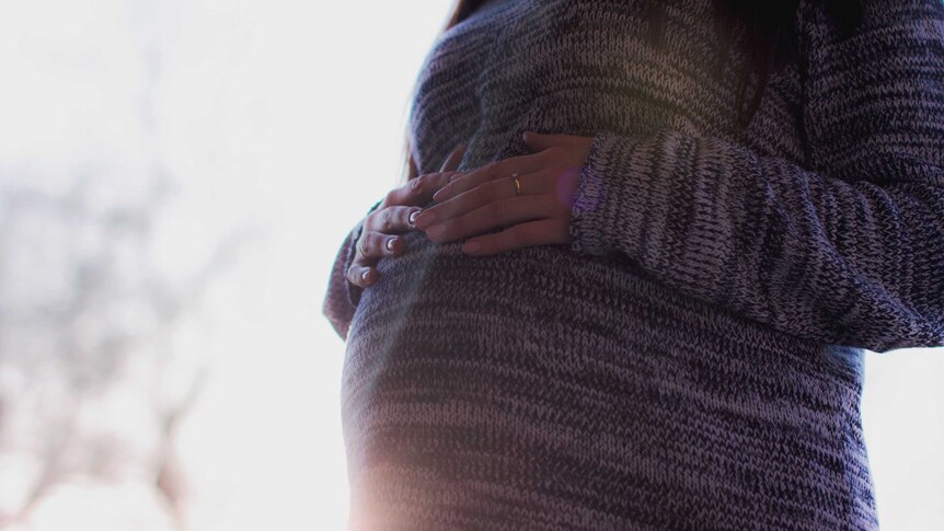 A close-up of a pregnant woman holding her stomach