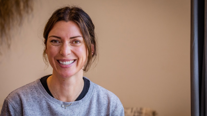 A head and shoulders shot of a woman in a grey jumper with brown hair in a pony tail.