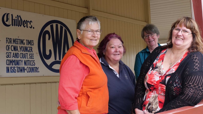 Six women stand on the balcony of an old Queenslander home, with a Childers QCWA sign on the wall behind them.