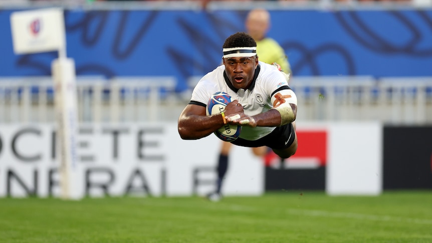 A man dives through the air before scoring a try.