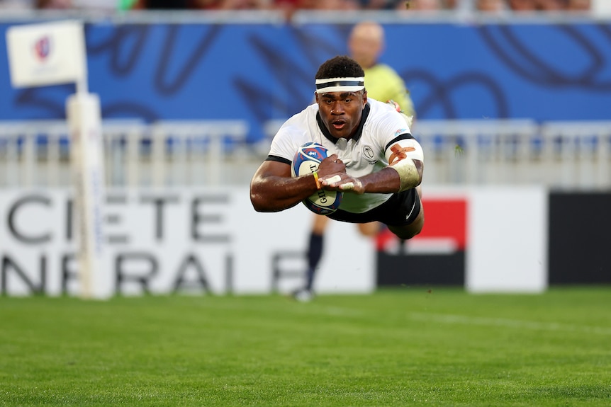 A man dives through the air before scoring a try.