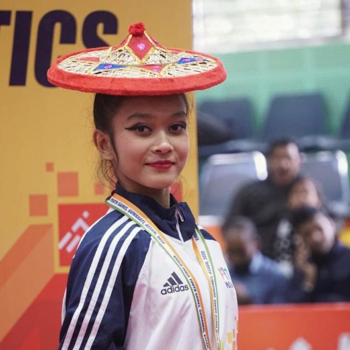 A close up picture of a teenage girl gymnast wearing a traditional hat, and a medal around her neck.
