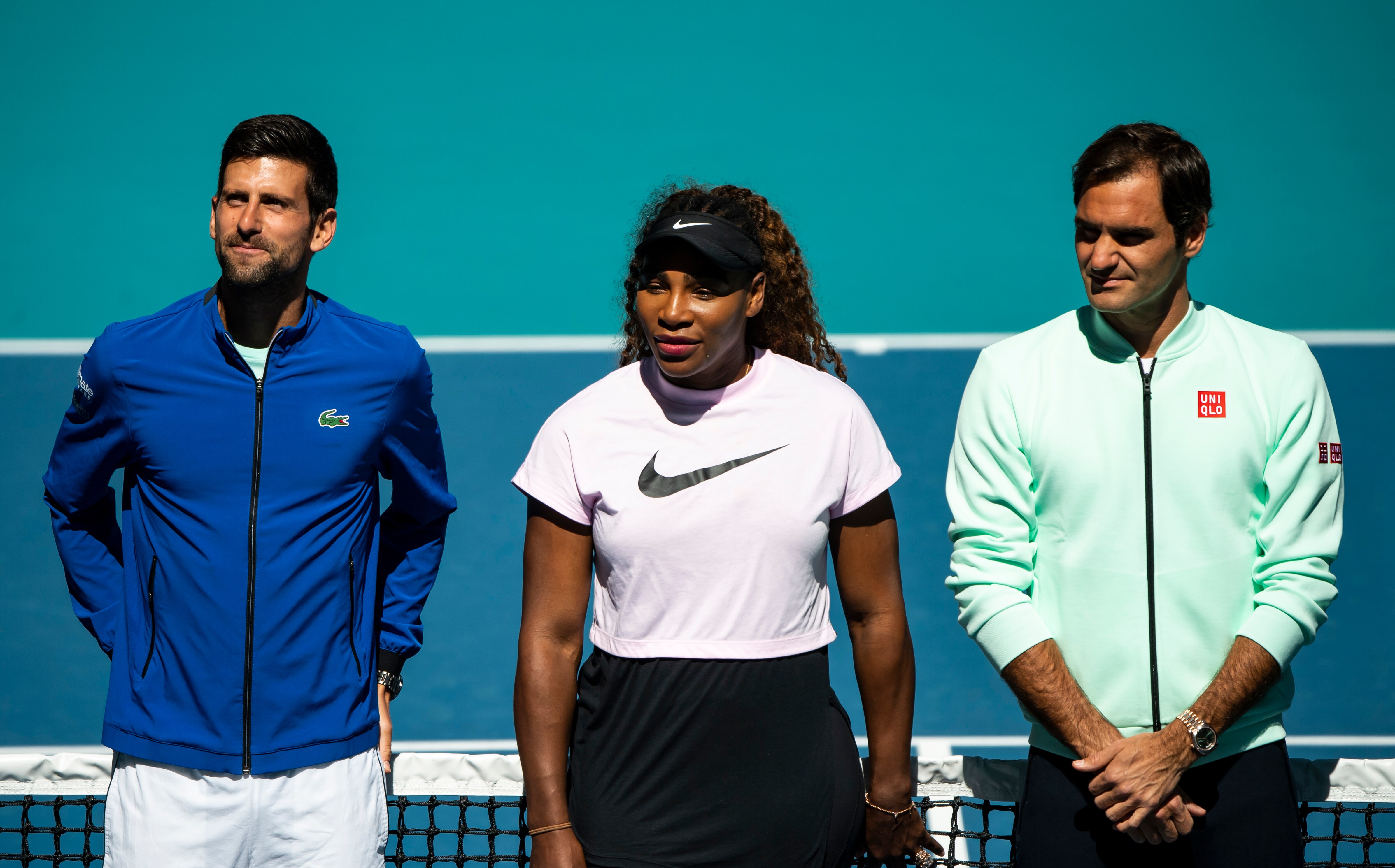 Novak Djokovic, Serena Williams and Roger Federer stand at the net on a tennis court.