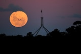 A bright red full moon is visible behind the top of Parliament House.