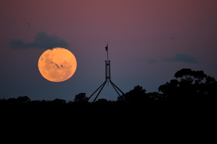 A bright red full moon is visible behind the top of Parliament House.