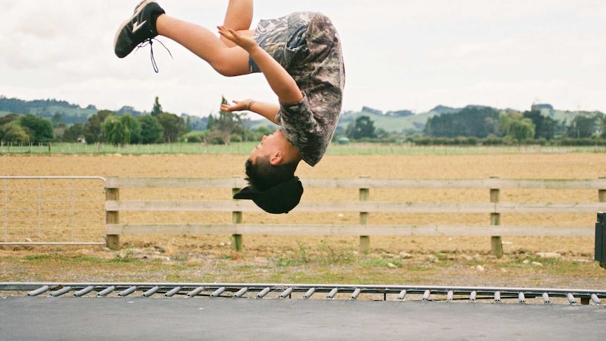A teenage child jumping upside down on a trampoline