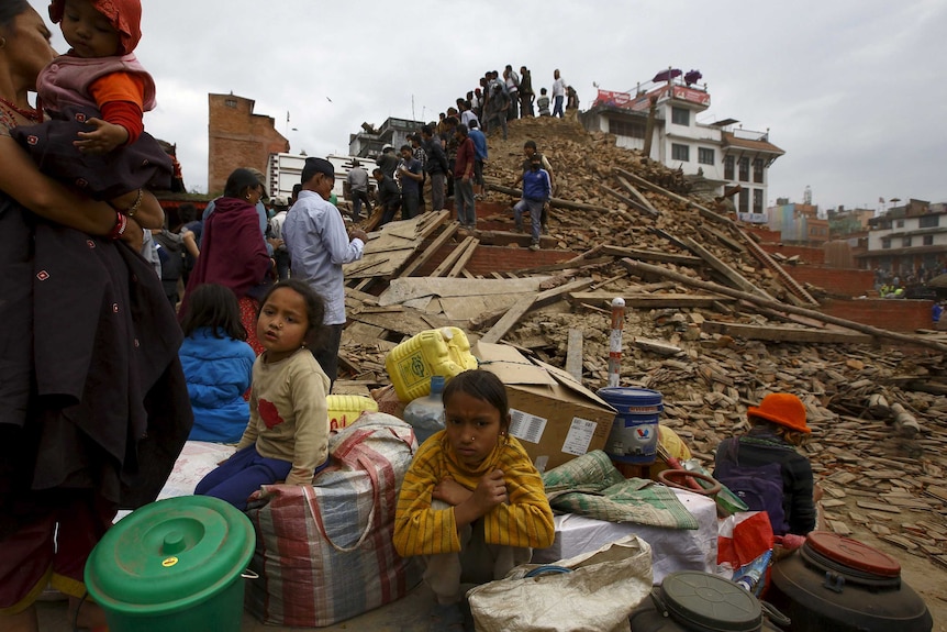 People sit with their belongings outside a damaged temple in Kathmandu