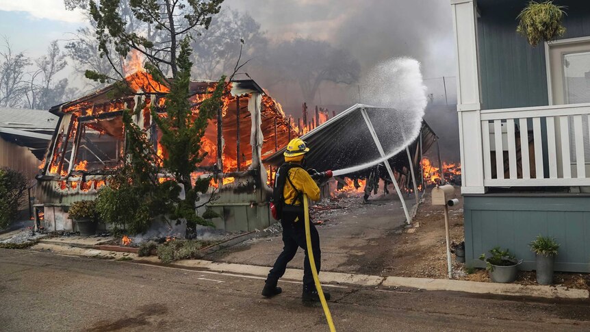 Firefighters battle flames at the Alpine Oaks Estates mobile home park. The structure is covered in fire, they are using hoses.