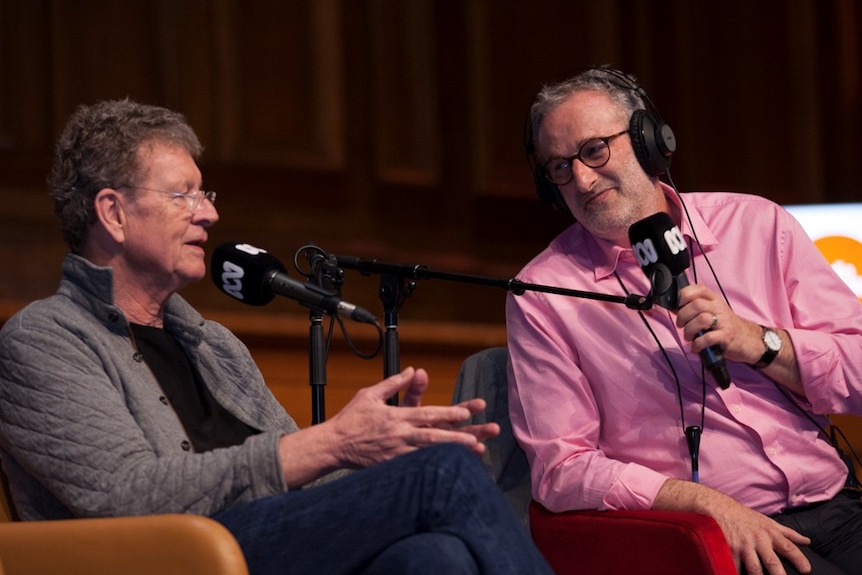 Red Symons and Jon Faine sit side-by-side on stage as they speak into ABC microphones.