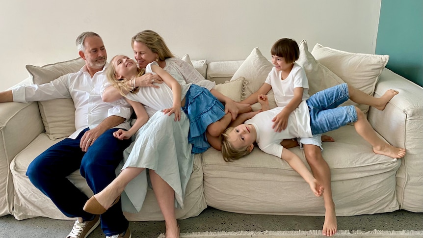 two parents and their three children pose together on a cream couch