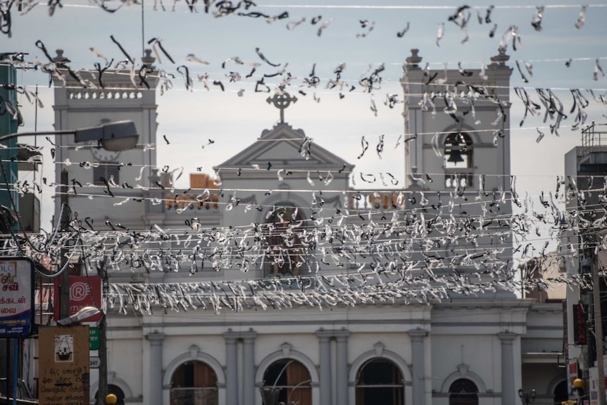 Lines and lines of black and white ribbons cross overhead in the street, with a church edifice in the background.