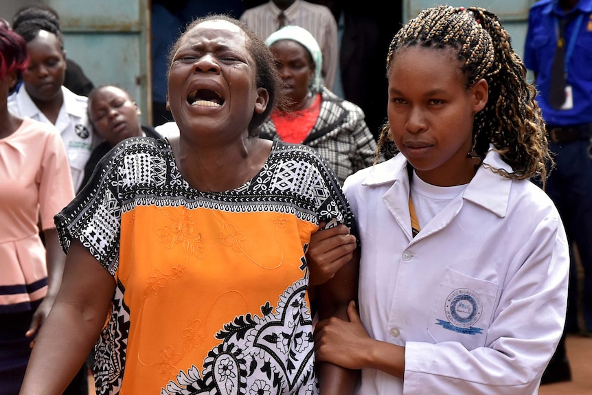 A woman screams as tears run down her face, her arm is held by a younger woman.