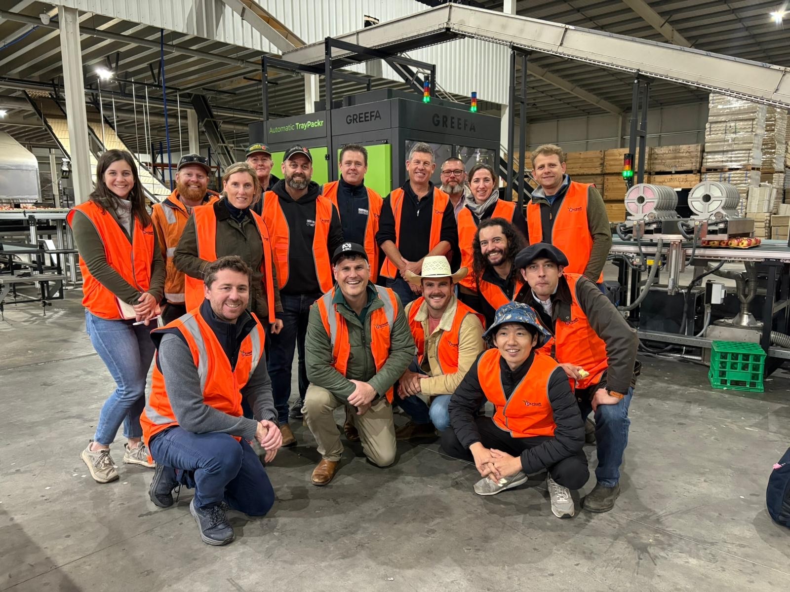 A group of people standing in high vis in a fruit packing shed.