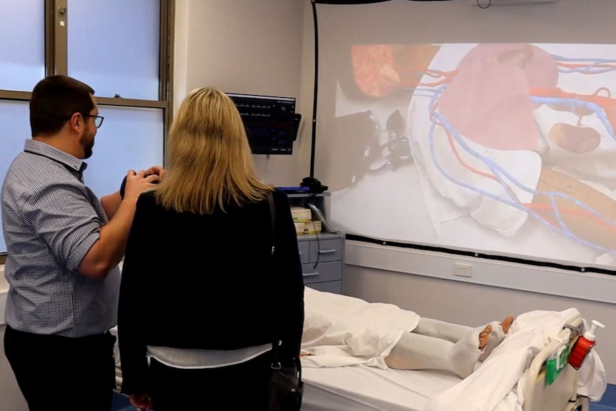 A man and a woman looking at a screen on which a dummy medical mannequin can be seen.