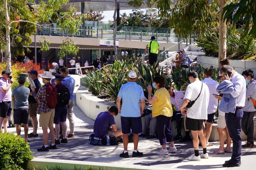 People with their backs to the camera queue in a line outside a hospital