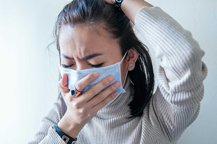 Young woman coughs into face mask.