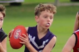 Young boy in an AFL match running with the ball.
