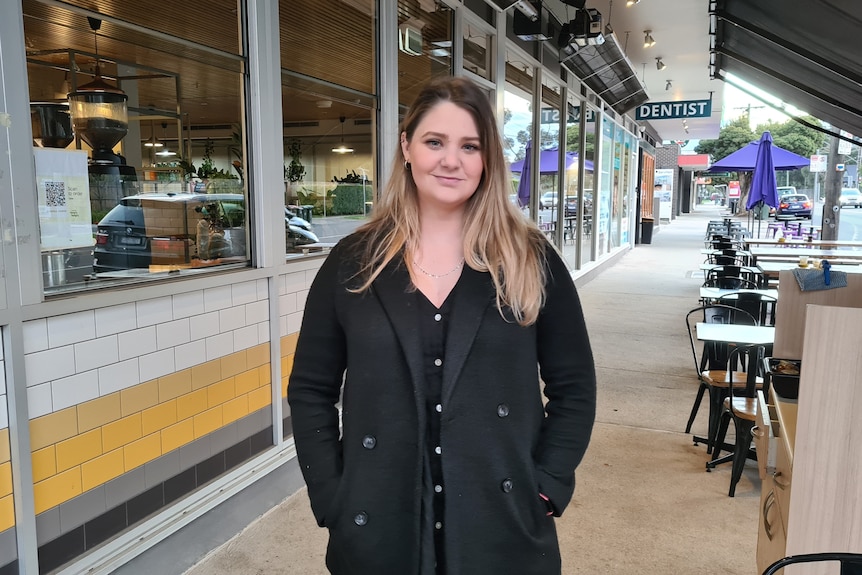 Sarah stands on a shopping strip in a black coat.