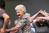A support worker guides an elderly lady through a dance.