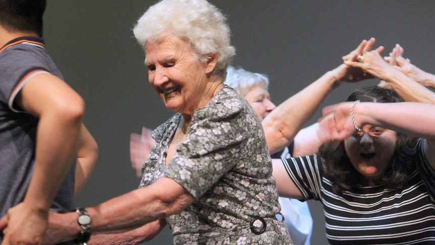 A support worker guides an elderly lady through a dance.