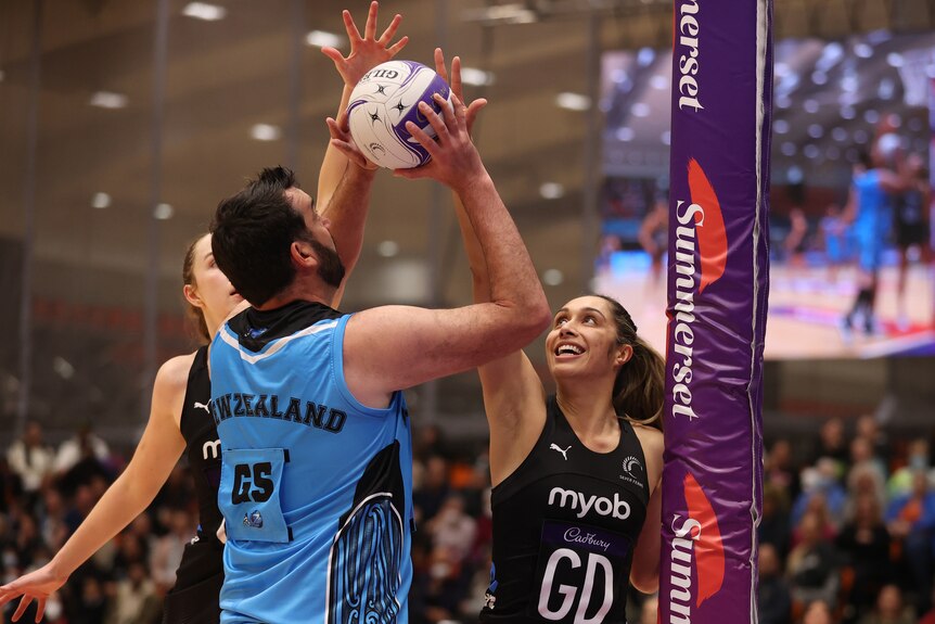 A New Zealand male player looks up to shoot as two New Zealand women's players defend