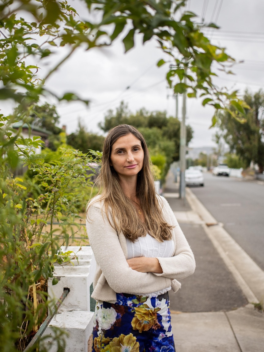 A woman stands on a street near a bush.