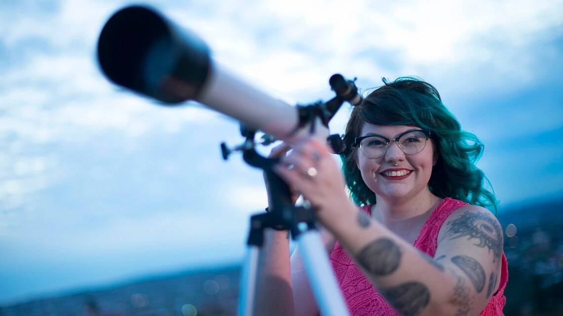 A woman holding a telescope and smiling at the camera.