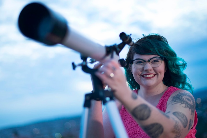 A woman holding a telescope and smiling at the camera.