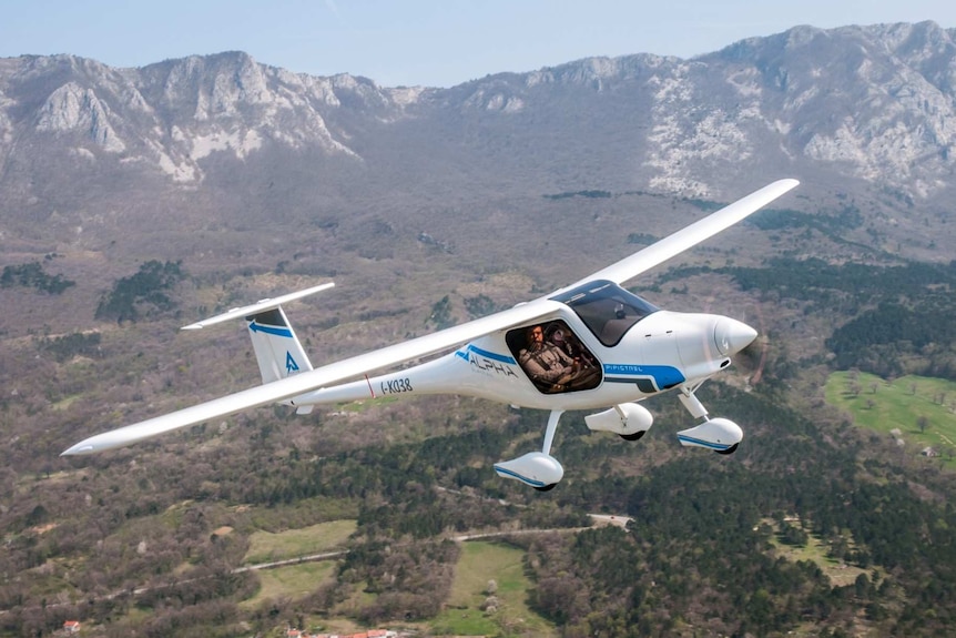 A small two-seater aeroplane in front of mountains