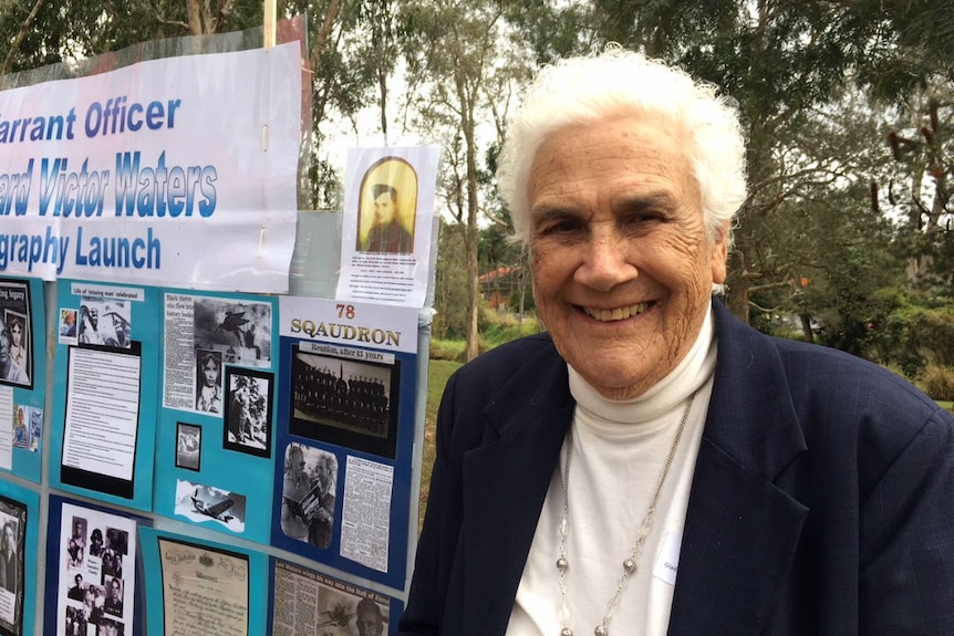 An older woman with white hair stands in front of an information board.