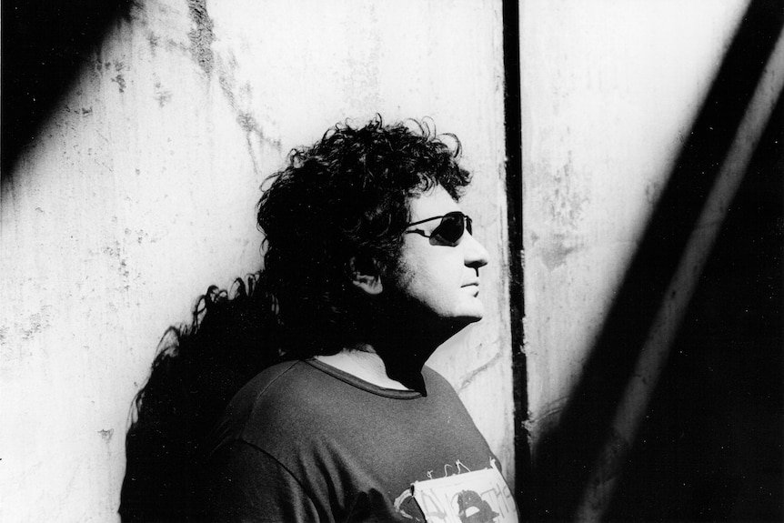A black and white photo of a man wearing a t-shirt and dark sunglasses