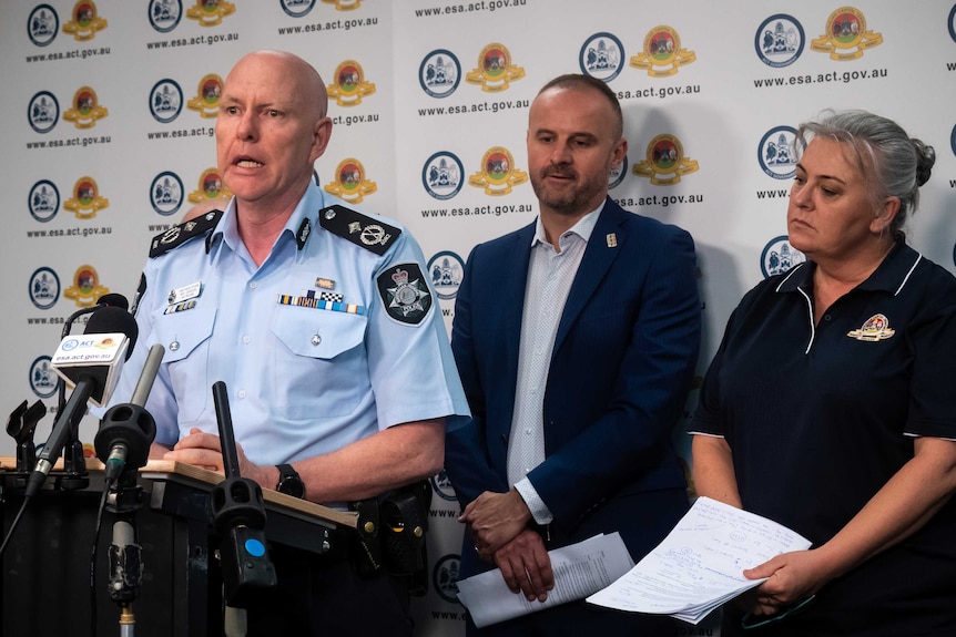 A police officer, a man in a suit and a woman in an ESA uniform face a press conference.