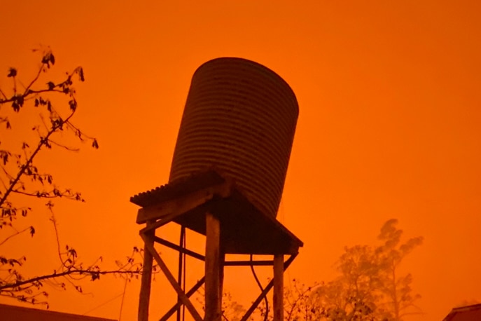 Water tank askew on a tall stand in the orange glow of fires
